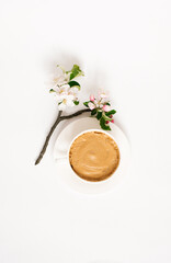 Cup of coffee with foam in a white porcelain and a branch of apple blossoms on a white background