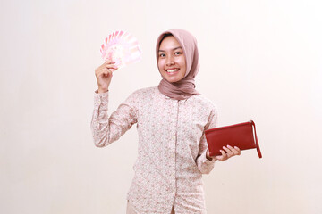 Happy young asian muslim girl standing while holding Indonesian banknotes. Isolated on white