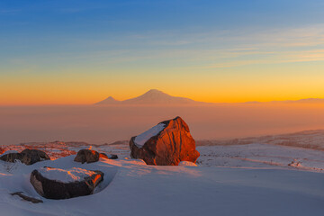 Sunset over the Ararat mountains  with large boulder in the foreground at winter as seen from the Aragats. Travel destination Armenia