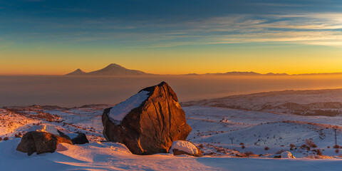 Wide angle view on sunset over the Ararat mountains  with large boulder in the foreground at winter as seen from the Aragats. Travel destination Armenia