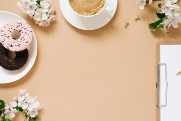 Blogger's flat lay. A cup of coffee, donuts, apple blossoms, a tablet on a beige background with a copy space