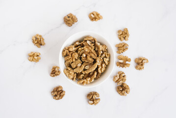 Walnut in a white bowl and are scattered on a marble table