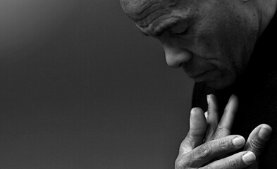 man praying to god with hands together Caribbean man praying with black background with people...