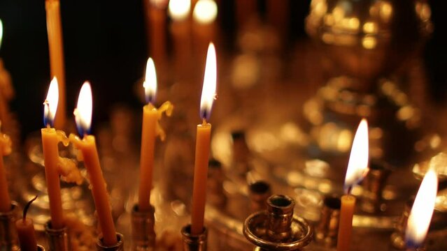 Close up burning candles in the Orthodox church. Memorial wax candles flicker with fire flame on large gold candlestick in the temple against dark. Concept of religion and faith in god