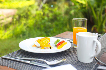 Sandwich with open poached egg and pepper on a plate and coffee with juice on the table