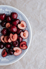 red cherries whole and halves on a plate with a blue pattern. background made of crumpled paper, shot from above
