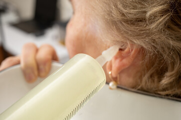 Office of an otolaryngologist, washing the ear of an elderly woman with water with a large...