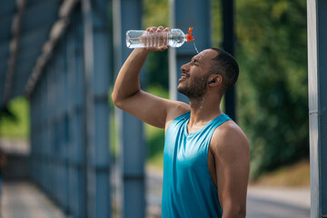Young dark-skinned athlete pouring some refreshing water on himself after workout