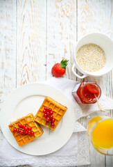 Waffles with red currant jam and berries, orange juice and oat flakes oatmeal