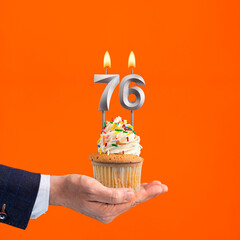Hand holding birthday cupcake with number 76 candle - background orange