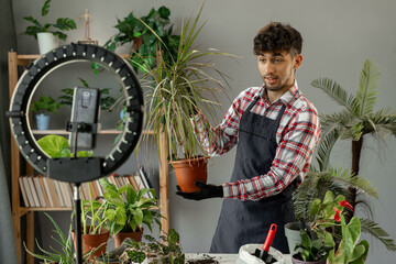 Working online influencer on social media concept. Young blogger man recording video of home garden...