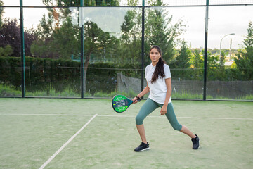 Young woman playing on padel court with racket	