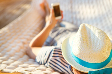 Man in hat in a hammock with mobile phone on a summer day