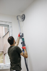 A man renovating a room. He smoothes the walls with a machine. Renovation and painting.