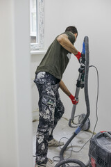 A man renovating a room. He smoothes the walls with a machine.