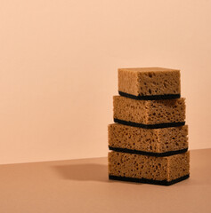 Brown dishwashing sponges lay one on top of the other on a beige background. Copy space for text.