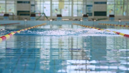 Front view of a powerful male swimmer using butterfly style for swimming in an indoor pool, arms and head movement, breathing technique, slow motion shot.
