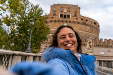 happy middle aged woman on vacation taking a selfie in front of castel sant'angelo fortress in rome - obrazy, fototapety, plakaty