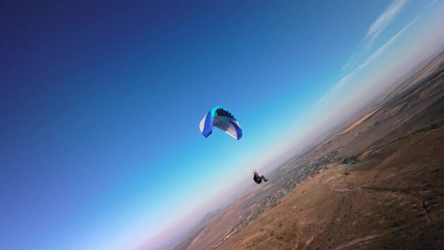 Aerial view from a sports FPV drone. A paraglider athlete flies near the slopes of a small mountain. Free paragliding flight over rural fields in autumn Video from FPV drone