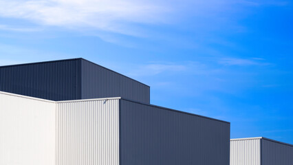 Modern black and white metal industrial factory buildings in minimal style against blue sky background, perspective side view
