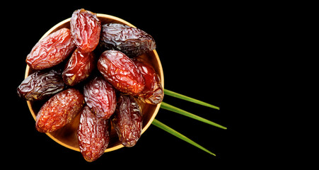 Dates fruit. Date fruits with palm tree leaf, in a wooden bowl, on black background. Medjool dates close up. Top view