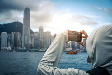 An Asian woman holds a mobile phone to take photos of modern architecture in Hong Kong