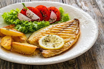 Grilled sea bream with potatoes and fresh vegetables on wooden table
