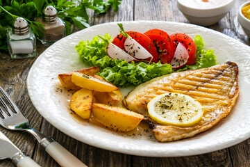 Grilled sea bream with potatoes and fresh vegetables on wooden table
