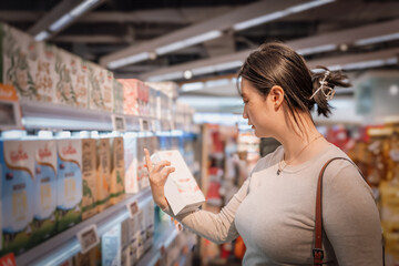A young and beautiful Asian girl is shopping in a supermarket, picking fresh milk from the dairy...