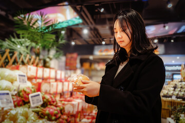Young Asian girl buys fresh fruits in the fruit and vegetable section of the supermarket, adopts a healthy diet and lifestyle and chooses healthier food.