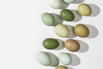 Natural Colorful Easter eggs close up, shadow at sunlight, white light background, copy space. Chicken eggs with nature colored eggshells, food Easter concept, top view, aesthetic flat lay