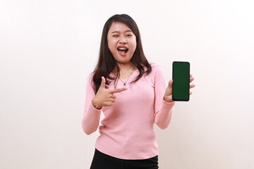 Naklejka premium Excited young asian girl standing while pointing a blank cell phone screen. Isolated on white background