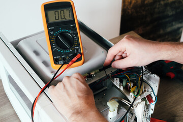 Diagnostics repair of microwave oven. A repair engineer uses a multimeter to check the circuits of...
