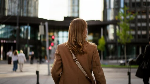 Back view of the stylish businesswoman strolling at business district while going to work