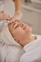Obraz na płótnie Canvas Facial treatment, Aesthetic services, Skincare consultation. Skilled esthetician gently massages face relaxed female client during soothing facial treatment in clean and bright clinical setting.