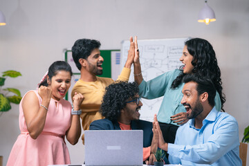 Group of team members celebrating success after seeing received mail from the laptop at office -...