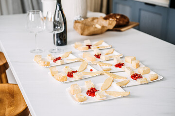 Preparing Appetizers with Wine for a Gathering. Unfocused hands arranging cheese and bread appetizers on a marble counter, with an empty wine bottle and glasses in the foreground.