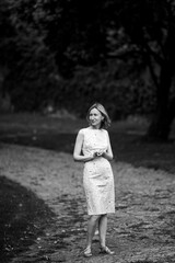 A woman stands waiting in the park. Black and white photo.