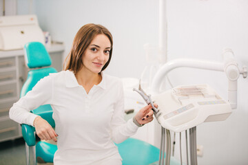 Young female dentist holds instruments in her hands in the interior of a modern dental clinic. The concept of professional activity, dental instruments and services.