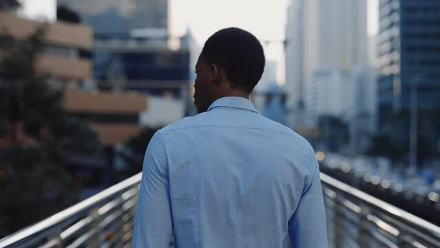 Back View of Young Successful African American Man in Shirt Walking Across Bridge in Business District. The Back of Businessman Walking Through the City on Way to Work. People Concept