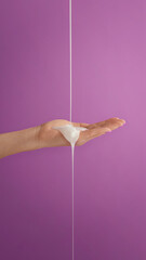 Textura crema cayendo en la mano, sobre fondo violeta