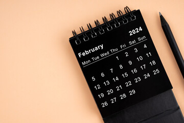 February 2024 Black spiral desktop calendar and wooden pencil.