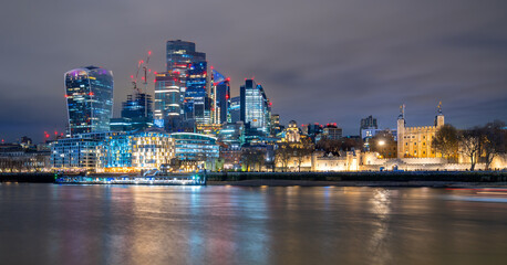 Night time panorama with the skyline of modern City of London, Thames river and tower castle with colorful illumination and water reflection. Capital of England with landmarks, sights at Tower Bridge