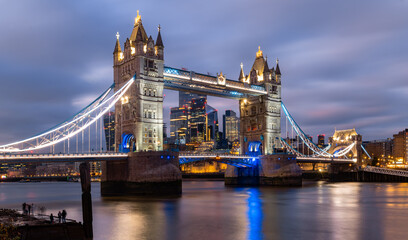 Fototapeta na wymiar Iconic Tower Bridge in London spanning over river Thames at evening twilight with colorful illumination at christmas time. Landmark, sight and tourist attraction in english metropole from river bank.