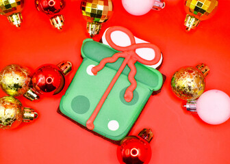 Imagen cenital de una galleta en forma de regalo sobre un fondo rojo navideño con esferas 