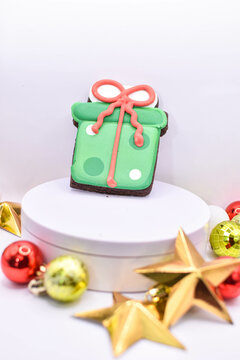 Imagen navideña de un estante blanco con decoraciones de esferas y estrellas y al fondo un regalo de galleta 