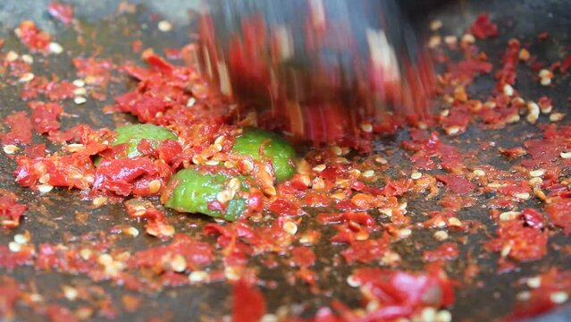 An asian hand pounding red chili and lime with stone mortar and pestle. Process to make sambal, an Indonesian condiment food