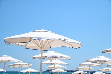 Fototapeta na wymiar White beach umbrellas on the seashore against the sky. Travel and recreation at sea.