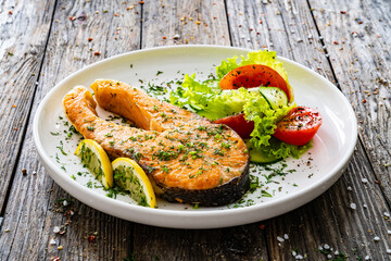Fried salmon steak and fresh vegetable salad served on wooden table
