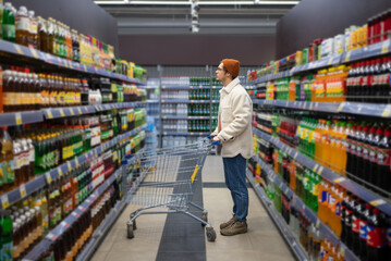 Man in store among racks of sodas. Young stylish millennial guy shopping in supermarket. Concept of huge selection of products, trip to hypermarket on sunday weekend. Promotions and discounts